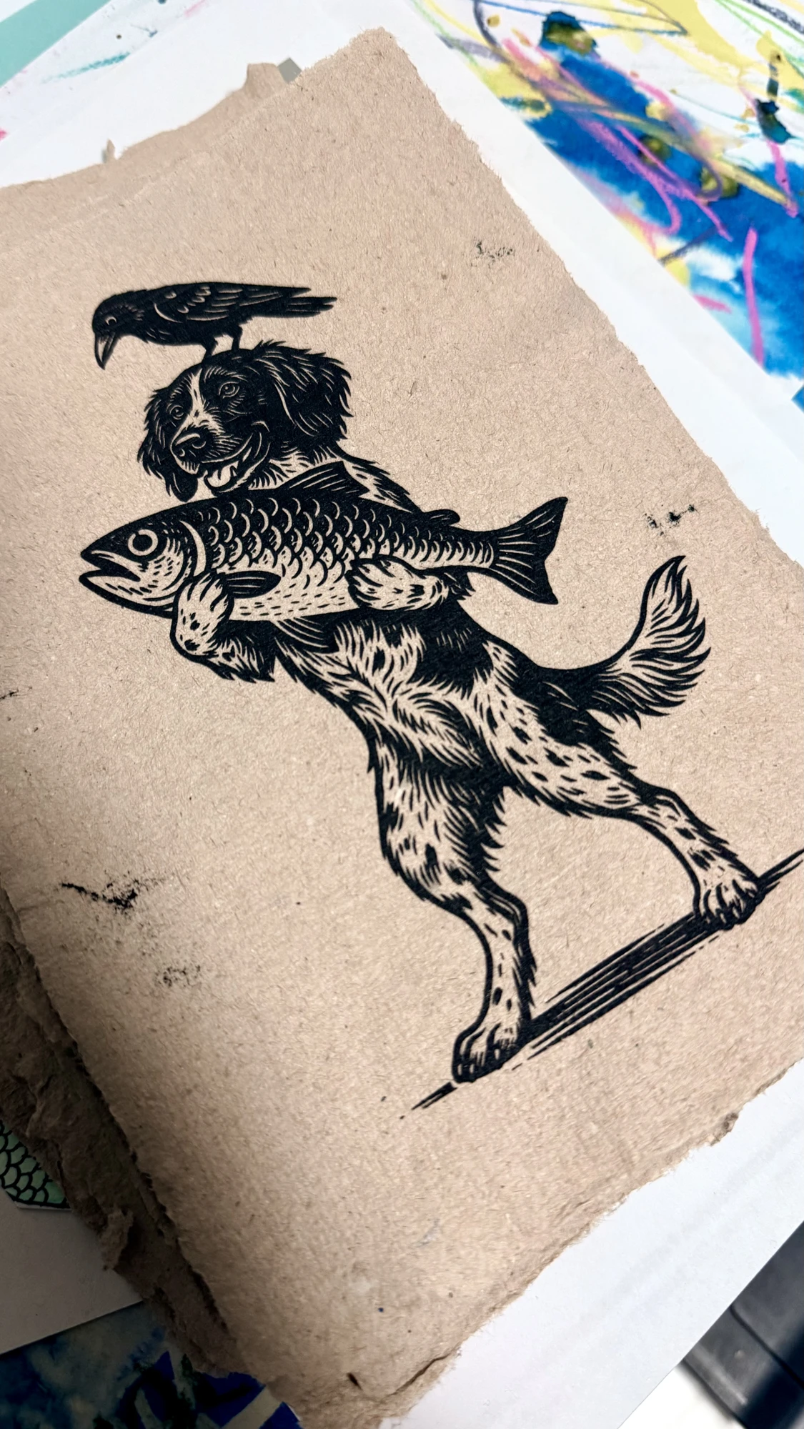 A black print of a dog carrying a fish, with a bird above its head, on natural paper.